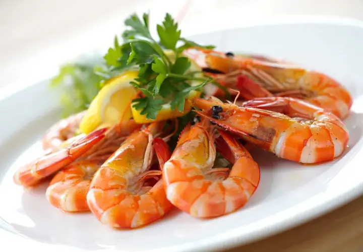 Un plato de gambas al ajillo, jugosas y doradas, adornado con perejil fresco y rodajas de limón. ¡Un manjar irresistible!