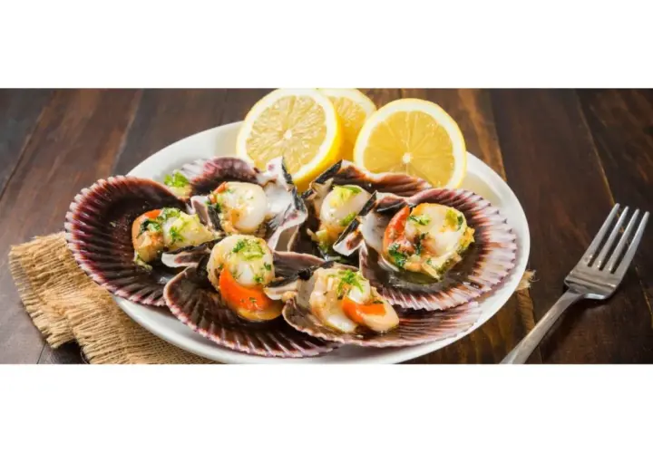 Zamburiñas a la plancha servidas en sus conchas, adornadas con perejil picado y rodajas de limón. Un plato delicioso y fresco.