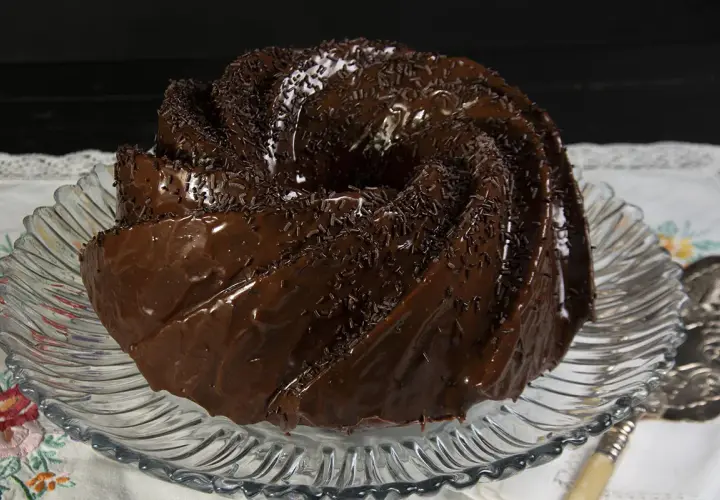 Bizcocho de chocolate glaseado y cubierto con chispas de chocolate, servido en un plato de cristal.