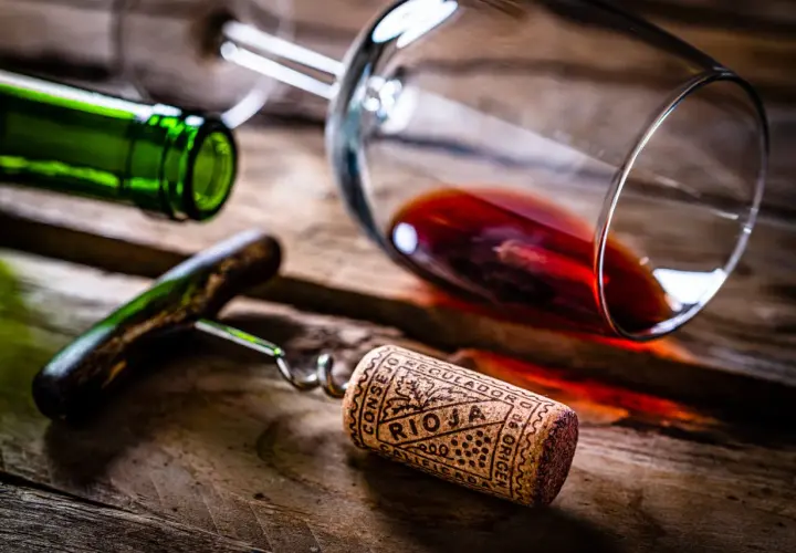 Tapón de corcho con la inscripción "Rioja" y "Calificación Añada", junto a una botella y copa de vino tinto sobre madera.