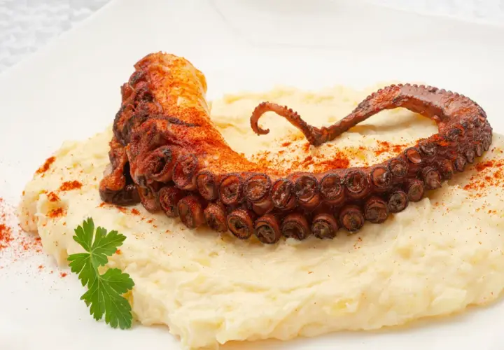 Delicioso pulpo a la plancha con puré cremoso, espolvoreado con pimentón y adornado con perejil fresco.