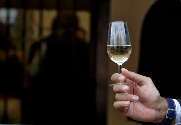 Mano sostiene copa de vino fino y manzanilla, con reflejos en el cristal.