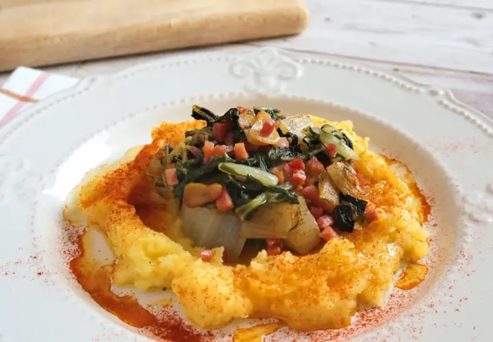 Puré cremoso de patatas con un sofrito de acelgas y trocitos de jamón, espolvoreado con pimentón.