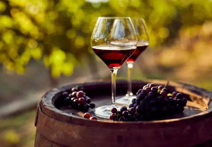 Dos copas de vino tinto y uvas moradas sobre un barril de madera, evocando las mejores añadas de vino.