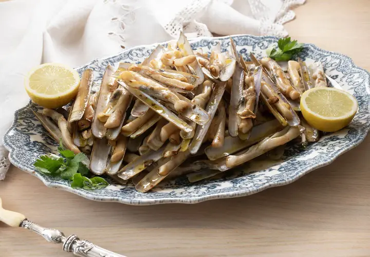 Deliciosas navajas a la plancha servidas en una fuente con limón y perejil.