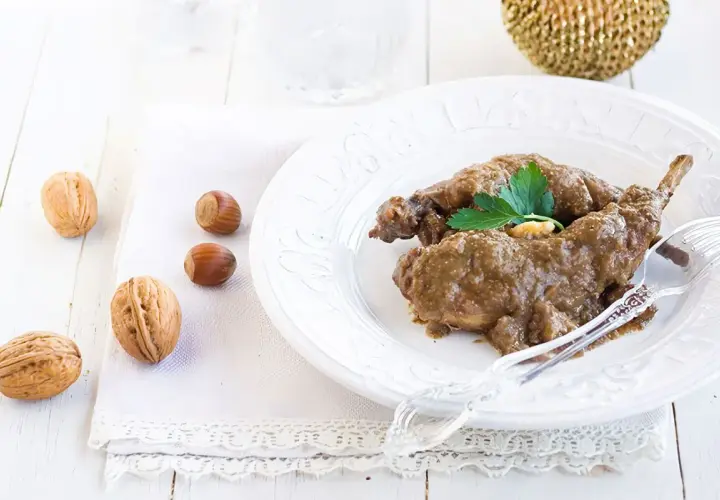 Delicioso conejo al ajillo servido en un plato blanco, acompañado de nueces y avellanas.