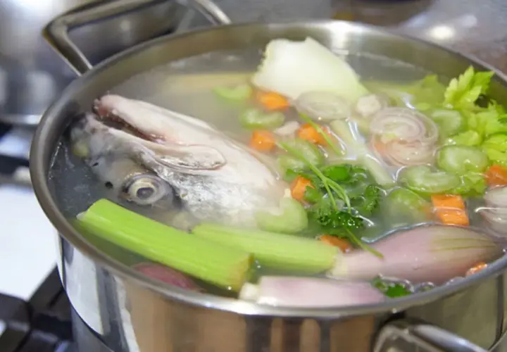 Cabeza de pescado y verduras hirviendo en una olla para hacer un delicioso caldo de pescado casero.