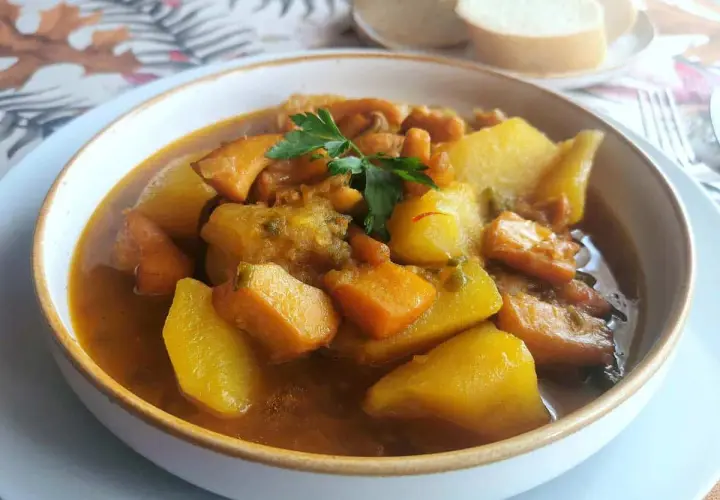 Un reconfortante plato de sepia con patatas, trozos de patata y zanahoria en una sabrosa salsa, adornado con perejil fresco.