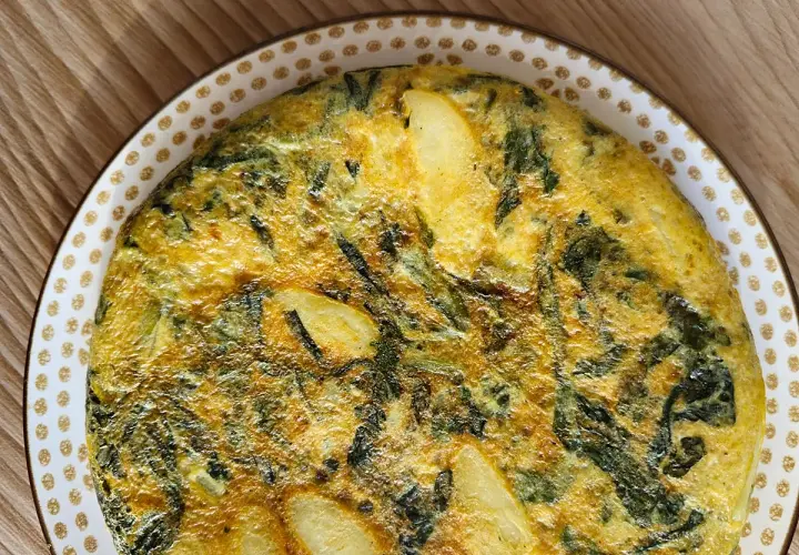 Tortilla de acelgas casera, dorada y jugosa, con trozos de patata y hojas verdes integradas en el huevo.