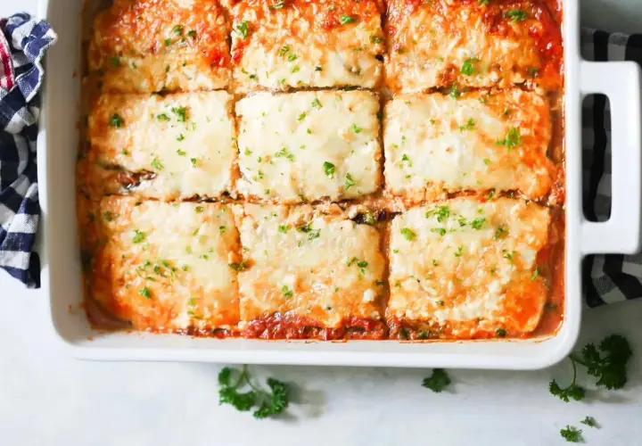 Lasaña de berenjena recién horneada, cubierta de queso derretido y perejil fresco, lista para servir.