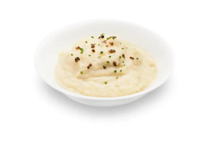 Un cremoso parmentier de patata, adornado con trocitos de bacon crujiente y cebollino fresco.