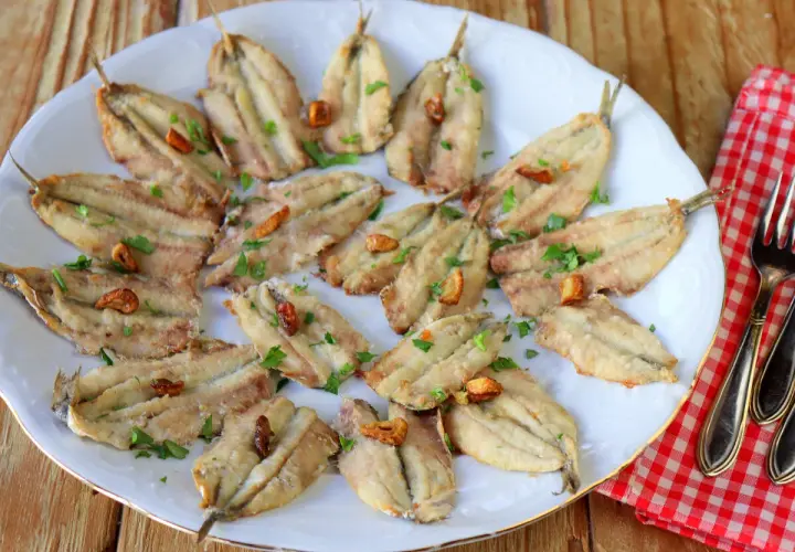 Boquerones en freidora de aire, dorados y crujientes, servidos en plato blanco con perejil picado y ajos fritos. ¡Un manjar saludable!