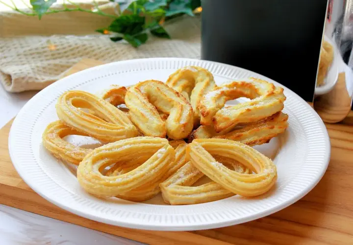 Plato blanco con churros caseros dorados y espolvoreados con azúcar. Perfectos para un antojo dulce.
