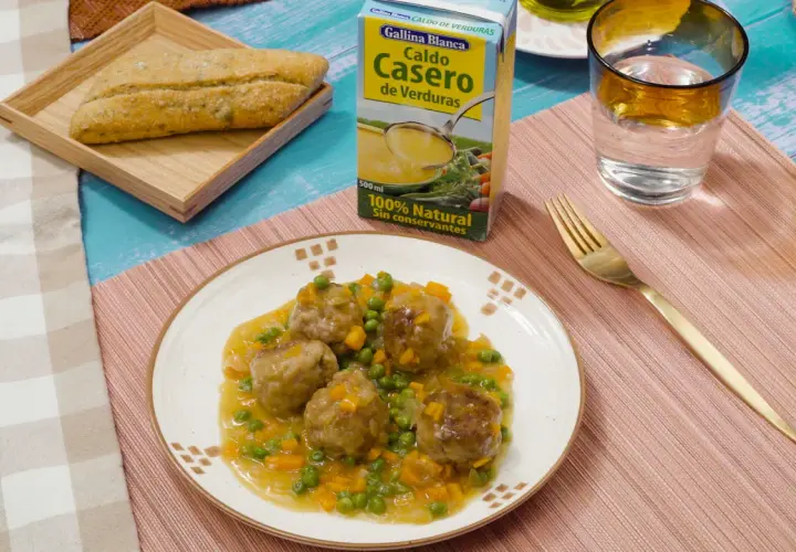 Albondigas a la jardinera en salsa con guisantes y zanahoria, acompañadas de pan y caldo de verduras.