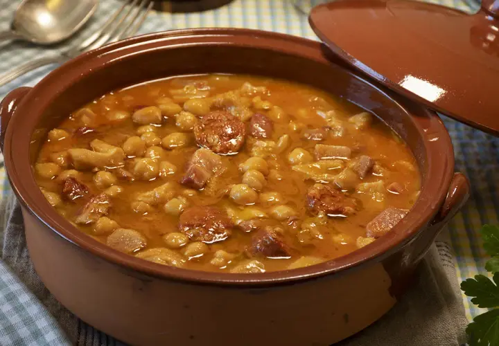 Un plato humeante de callos a la gallega, con garbanzos, chorizo y trozos de carne en una cazuela de barro.