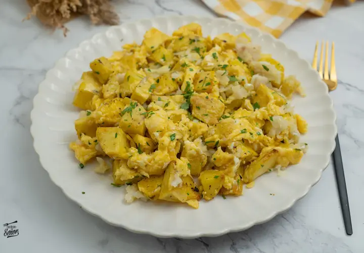 Un delicioso revuelto de bacalao con patatas, espolvoreado con perejil fresco. Un plato casero perfecto para cualquier momento del día.