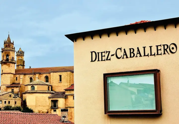 Edificio con el nombre "Diez-Caballero" en relieve, con una iglesia antigua al fondo.