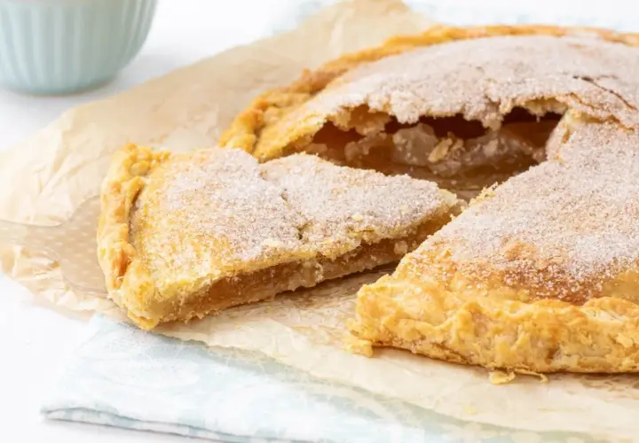 Un delicioso pastel cordobés, espolvoreado con azúcar, con una porción cortada mostrando su relleno dorado.
