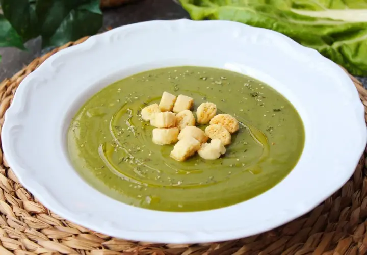 Crema de acelgas verde vibrante, servida en plato blanco con picatostes dorados y un chorrito de aceite de oliva.