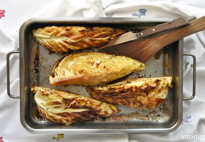 Cuatro gajos de col asada en una bandeja metálica, con hierbas y bordes dorados. Perfectas para tus recetas con col.