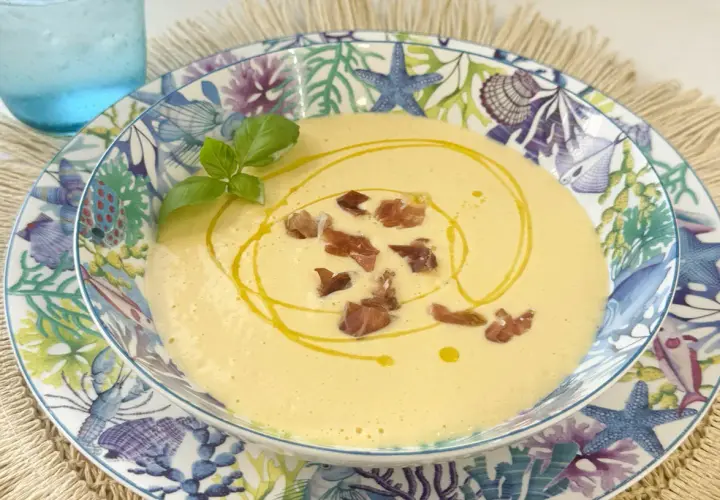 Deliciosa crema de espárragos, coronada con crujientes trocitos de jamón y un hilo de aceite de oliva. Servida en un plato con motivos marinos.
