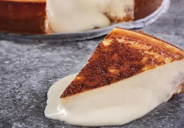 Una porción de tarta de queso cremosa, con la base dorada y el relleno blanco, se desliza sobre una salsa de queso.