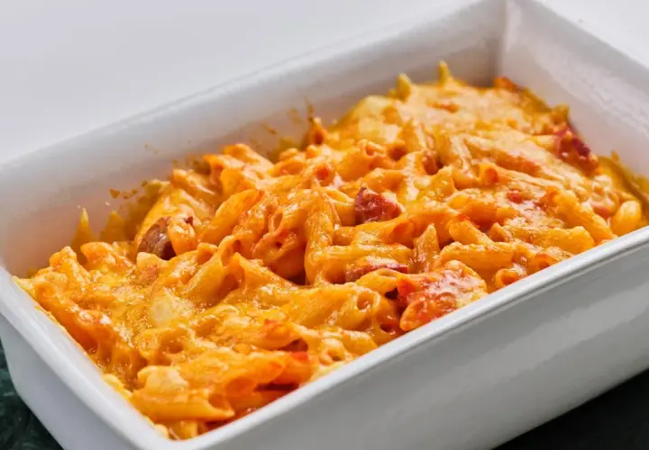 Macarrones con chorizo gratinados, cubiertos de queso derretido y burbujeante en una fuente blanca.