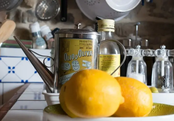 Aceite de oliva y limón para que sirve: una lata vintage de aceite de oliva italiano, limones frescos y molinillos de sal y pimienta en una cocina rústica.