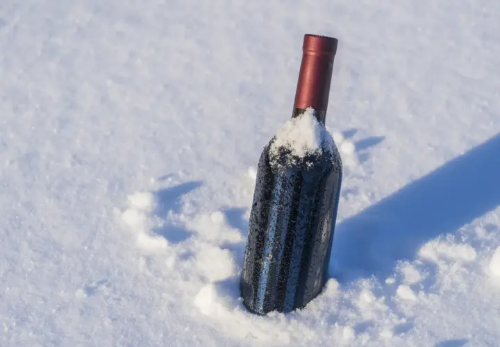 Botella de vino tinto cubierta de nieve, parece que el vino se congela en la nieve.