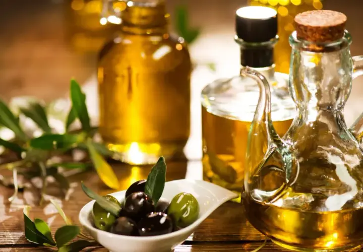Aceite de oliva dorado en botellas y jarra, con aceitunas frescas y ramas de olivo. Descubre las propiedades del aceite de oliva.