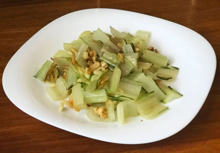 Pencas de acelgas salteadas con nueces, servidas en un plato blanco sobre una mesa de madera.