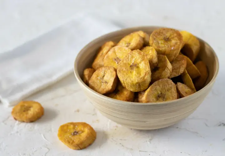 Un tazón de crujientes rodajas de plátano frito, espolvoreadas con sal, listas para disfrutar.