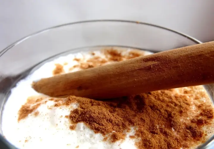 Vaso de leche merengada con canela en polvo y una rama de canela.