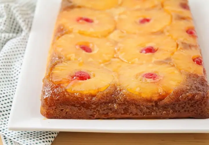 Tarta de piña dorada y brillante, con rodajas de piña caramelizada y cerezas rojas en cada centro. Un postre casero irresistible.