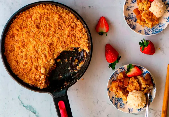 Crumble de manzana recién horneado en sartén, servido en platos con fresas y helado. ¡Un postre casero irresistible!