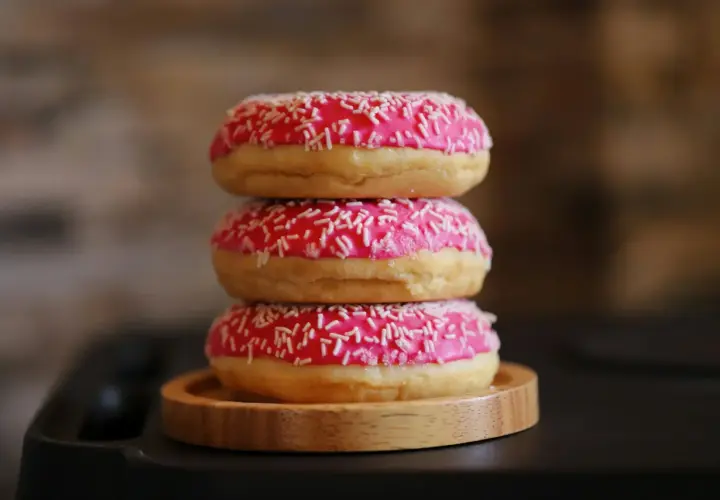 Tres deliciosos donuts caseros apilados, cubiertos con glaseado rosa brillante y chispas blancas.