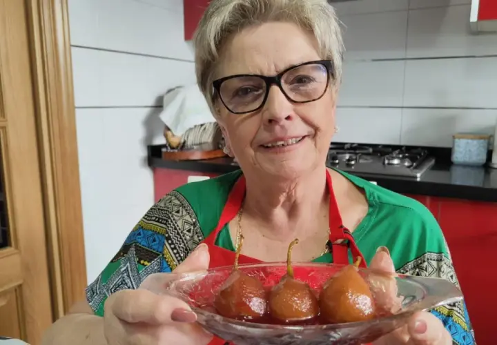 Mujer sonriente muestra un plato con peras al vino, un postre casero listo para disfrutar.