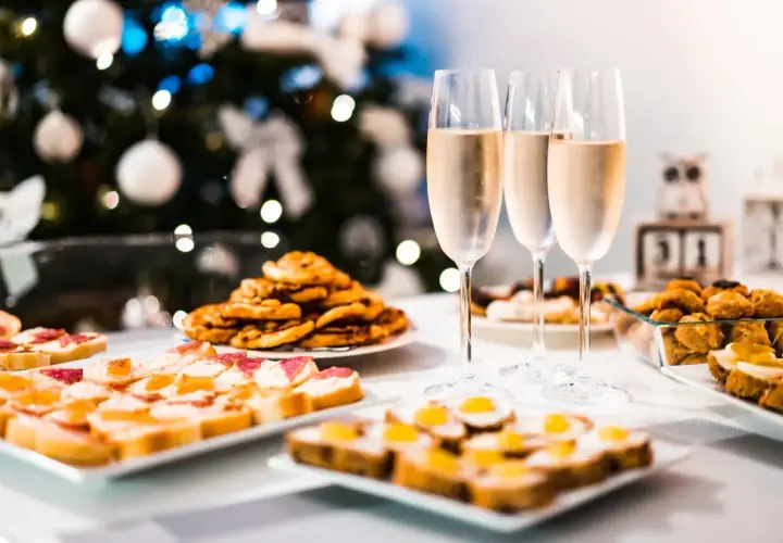 Copas de vino frizzante listas para brindar junto a aperitivos festivos, con un árbol de Navidad decorado al fondo.