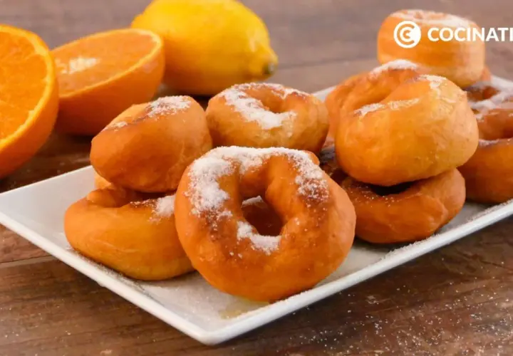 Rosquillas de naranja recién hechas, espolvoreadas con azúcar, junto a naranjas y un limón.