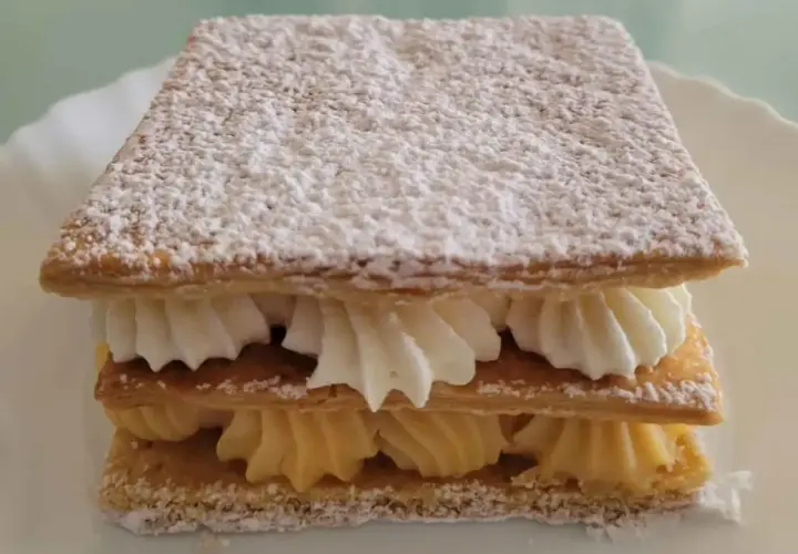 Delicioso milhojas de crema, con capas crujientes de hojaldre y rellenos de crema pastelera y nata montada, espolvoreado con azúcar glas.