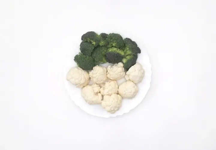Un plato blanco con un panache de verduras: brócoli verde y coliflor blanca, listos para cocinar.