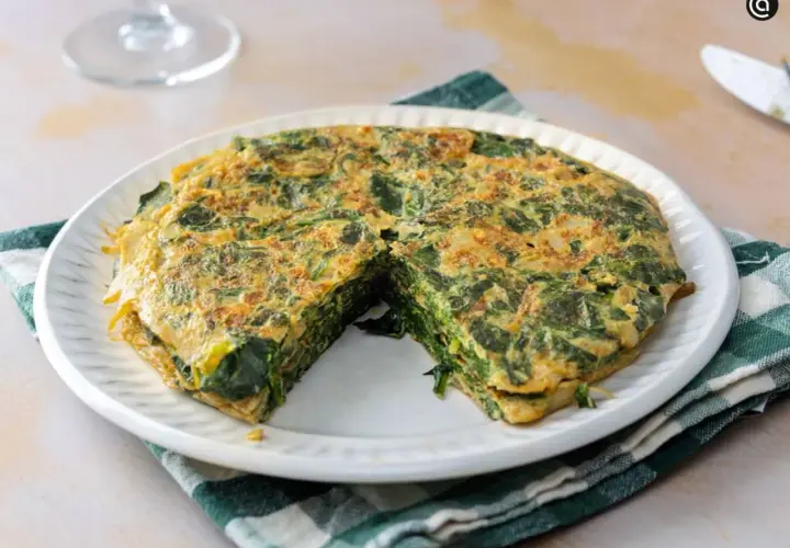 Tortilla de espinacas, jugosa y dorada, servida en plato blanco con servilleta a cuadros.