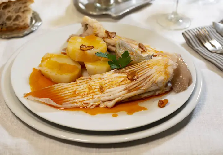Raya a la gallega servida con patatas cocidas y un toque de ajo frito.