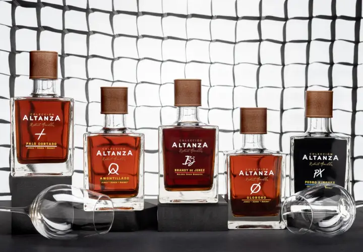 Cinco botellas de brandy de Jerez de la colección Altanza, incluyendo un amontillado, dispuestas sobre una superficie oscura con copas de vino vacías.