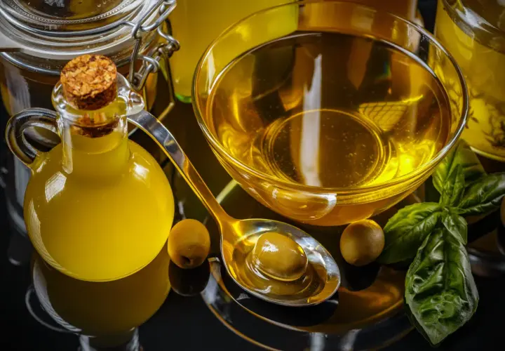Botella de aceite de oliva, cuenco con aceite, cuchara con aceituna y hojas de albahaca. El precio del aceite de oliva va a subir.