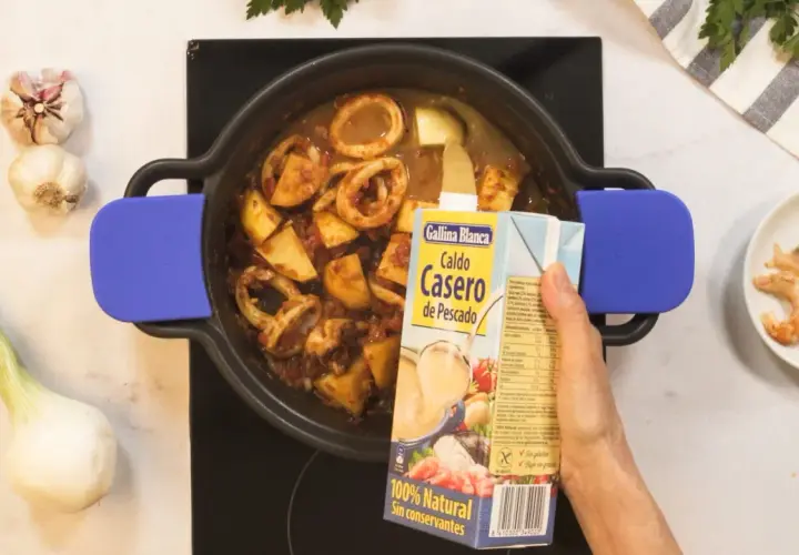 Se añade caldo de pescado a una cazuela con calamares y patatas, ingredientes para una deliciosa caldereta.