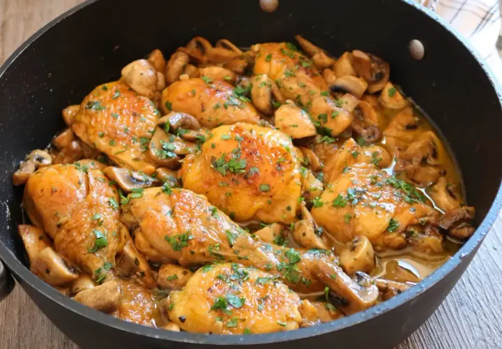 Pollo a la cerveza jugoso y dorado, con champiñones y perejil picado, servido en una sartén.