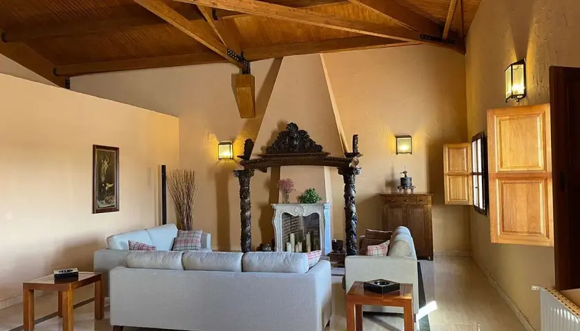 Salón acogedor en finca Los Aljibes, con chimenea rústica, sofás cómodos y vigas de madera en el techo.