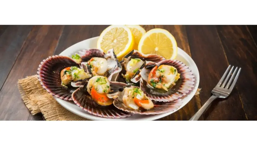 Zamburiñas a la plancha servidas en sus conchas, adornadas con perejil picado y rodajas de limón. Un plato delicioso y fresco.