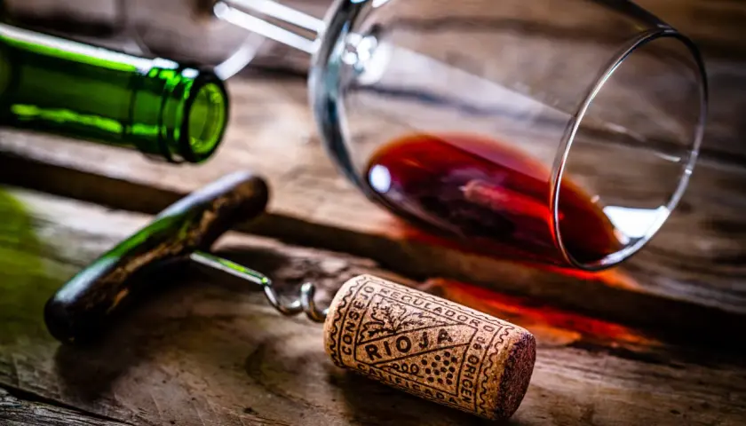 Tapón de corcho con la inscripción "Rioja" y "Calificación Añada", junto a una botella y copa de vino tinto sobre madera.